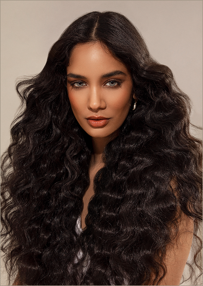 Woman with long, voluminous, wavy dark hair and light makeup, facing forward against a neutral background—showcasing a modern precision haircut and style from an eco-friendly beauty salon spa. - Garbo A Salon & Spa TX