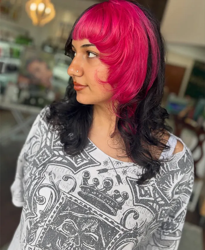 A woman with a modern precision haircut—shoulder-length black hair with vivid pink bangs and front layers, wearing a patterned gray and white top, looking to the side indoors. - Garbo A Salon & Spa TX
