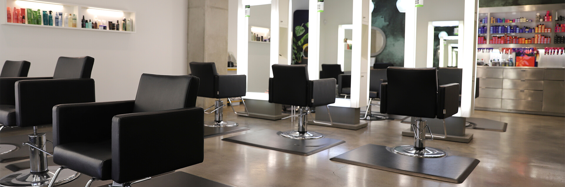 Modern hair salon offering modern precision haircut and style, with black styling chairs, large mirrors, shelves of hair products, and polished concrete floors—all well-lit and organized. - Garbo A Salon & Spa TX