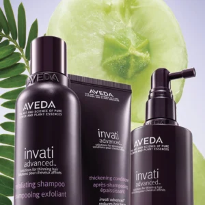 Three Aveda Invati Advanced hair care products are displayed with green leaves and a sliced green fruit in the background, reflecting the essence of an eco friendly beauty salon spa. - Garbo A Salon & Spa TX