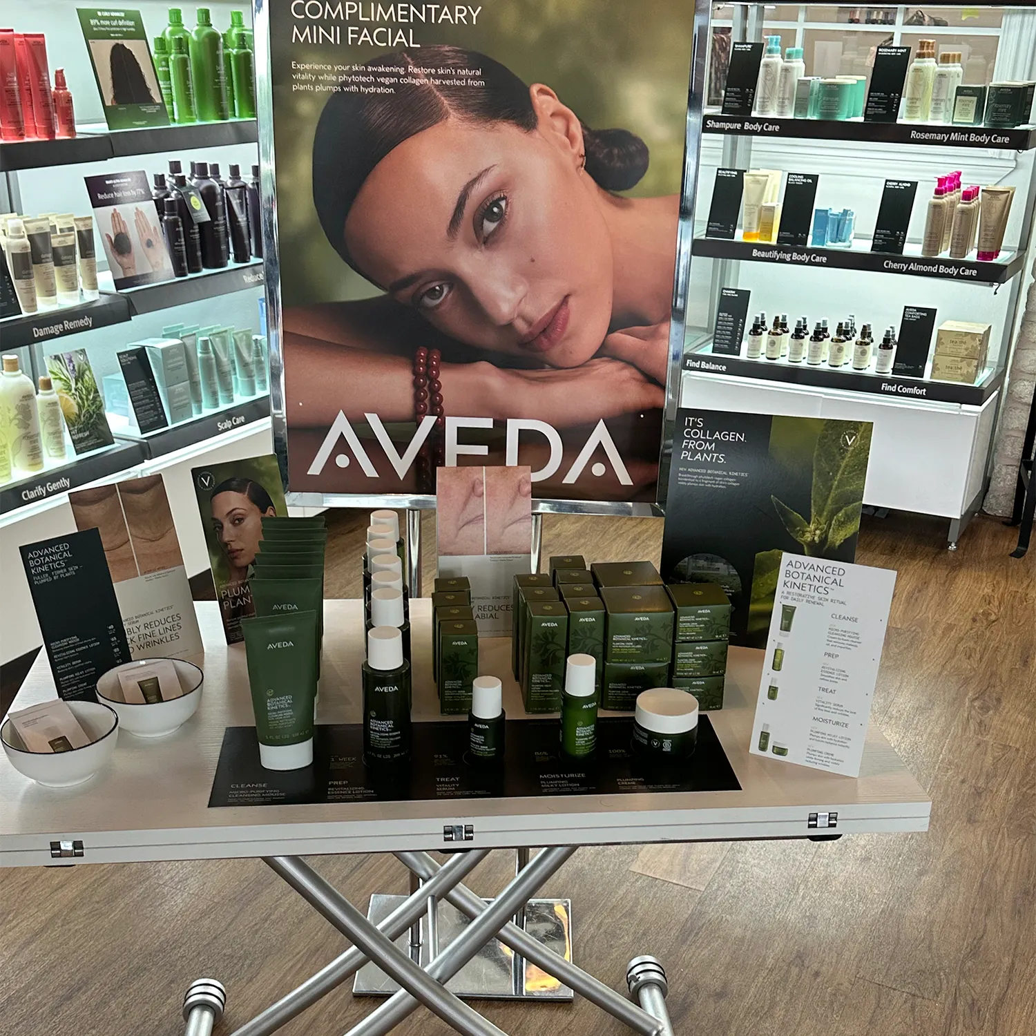 A display table with various Aveda skincare products and promotional materials for complimentary mini facials in a well-lit store. - Garbo A Salon & Spa TX
