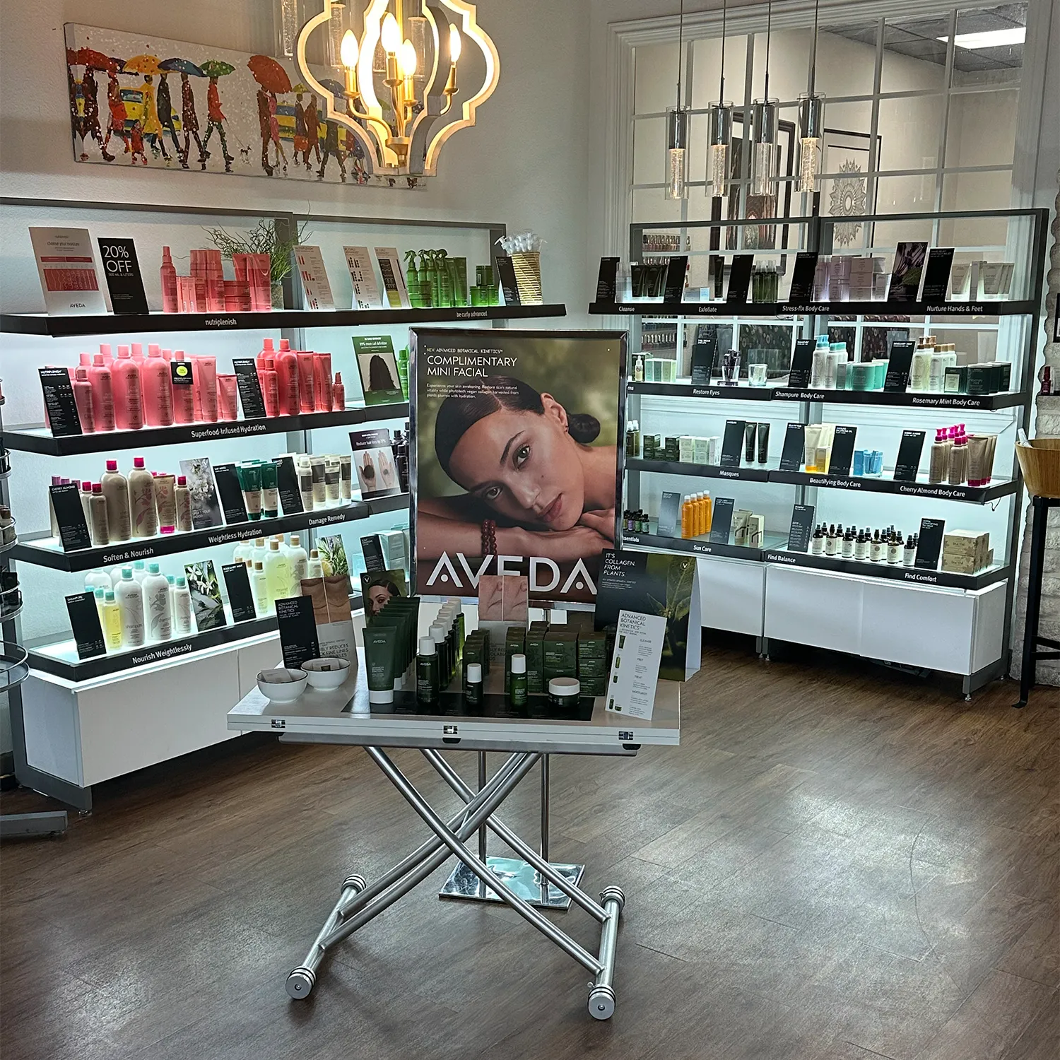 Display of Aveda skincare and haircare products in a well-lit salon with shelves of various beauty items and a promotional poster on a stand. - Garbo A Salon & Spa TX