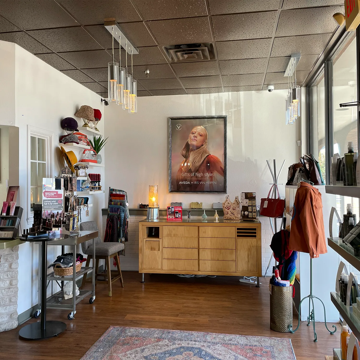 A boutique interior with hats, scarves, and accessories on display, modern hanging lights, a large portrait, and a wooden cabinet against the back wall. - Garbo A Salon & Spa TX