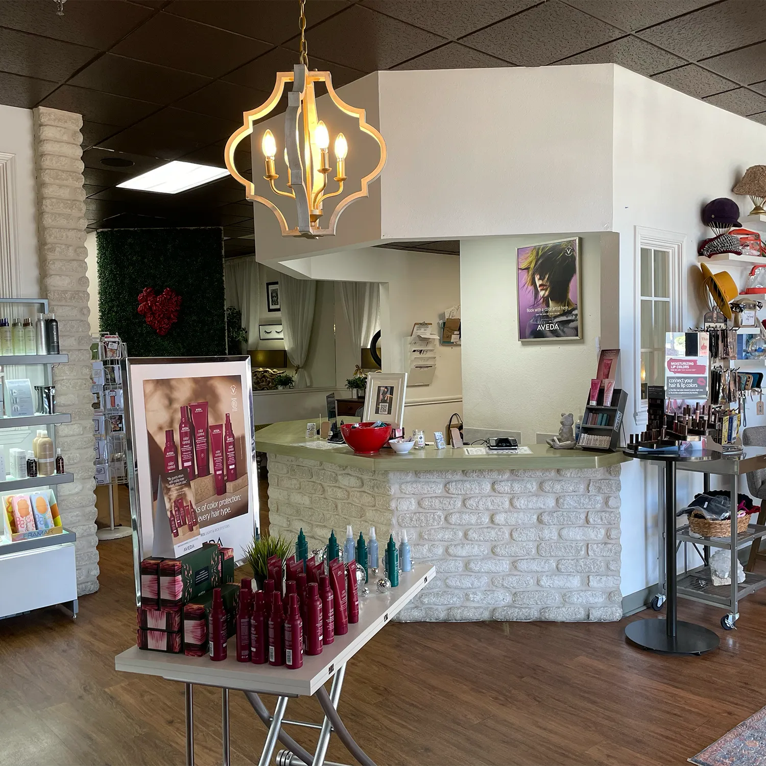 A well-lit salon interior with hair products on display, a chandelier overhead, a product counter in the back, and shelves with beauty items along the walls. - Garbo A Salon & Spa TX