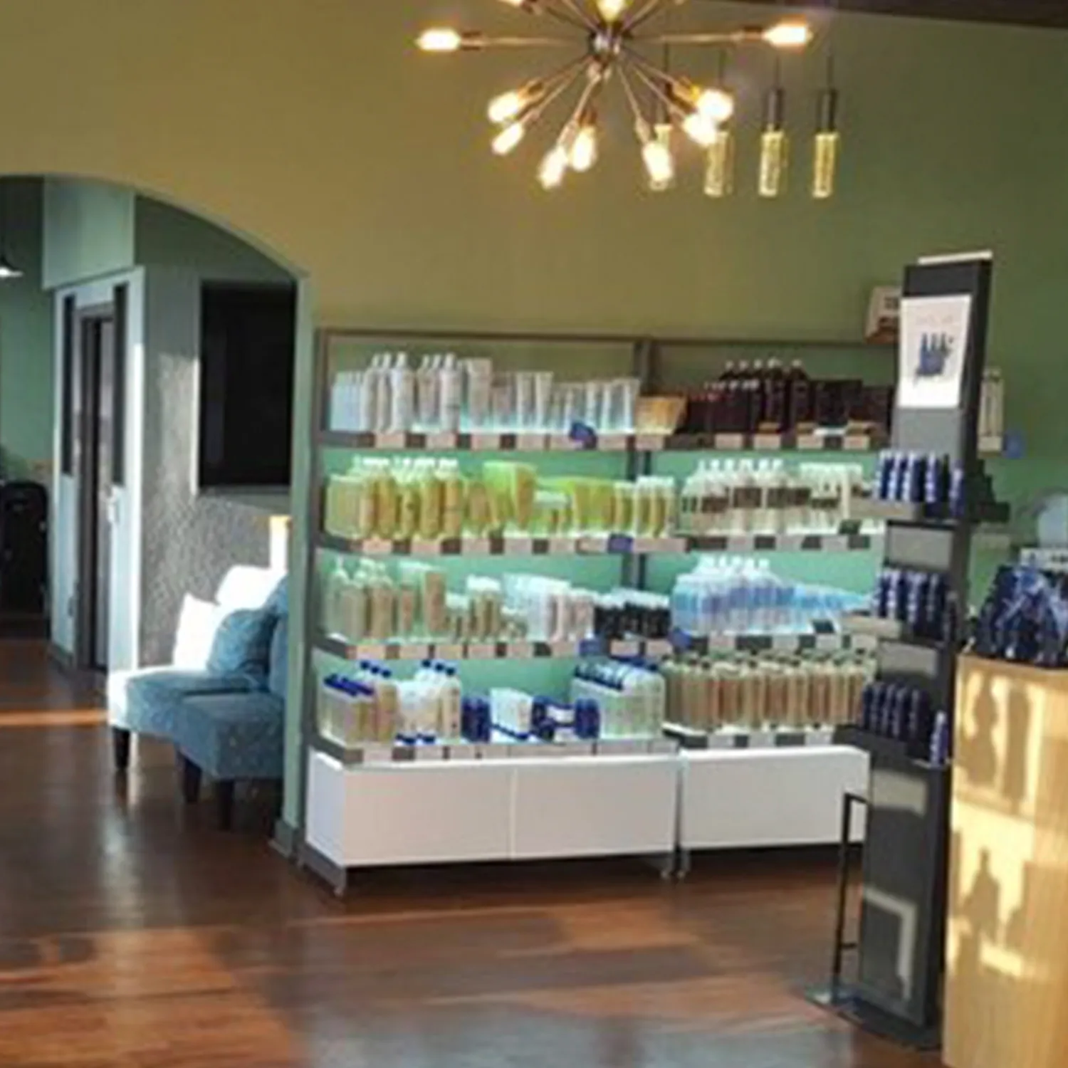 Shelves stocked with various bottles and containers of hair and beauty products in a well-lit salon with wooden floors and modern lighting. - Garbo A Salon & Spa TX