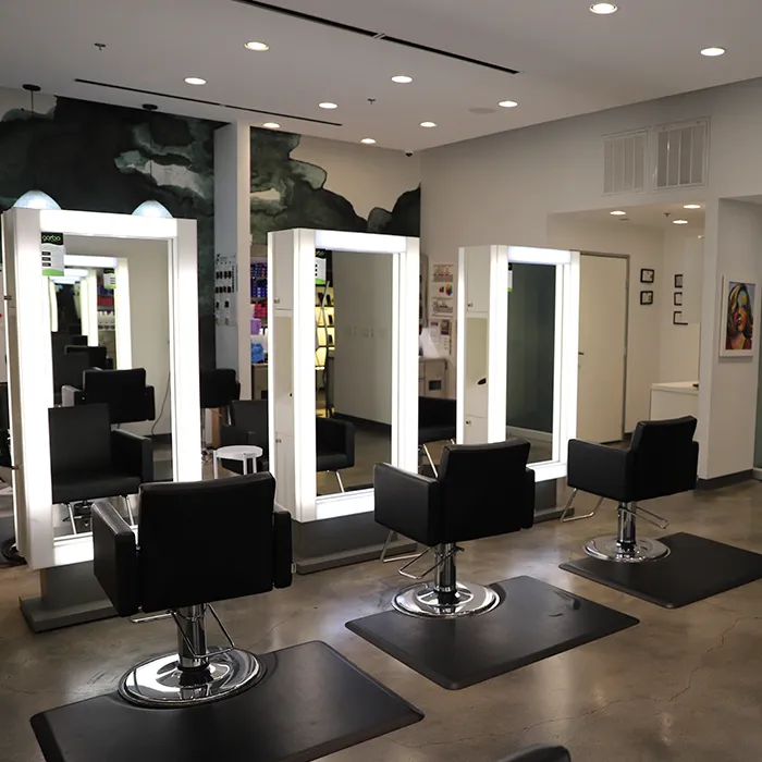 Three black salon chairs face large, illuminated mirrors in a modern, well-lit hair salon with polished concrete floors and minimalist decor. - Garbo A Salon & Spa TX