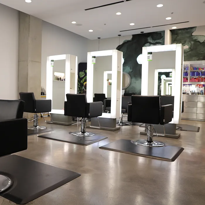 Modern hair salon interior with black styling chairs, large illuminated mirrors, and shelves with hair products; the space is clean and well-lit with polished concrete floors. - Garbo A Salon & Spa TX