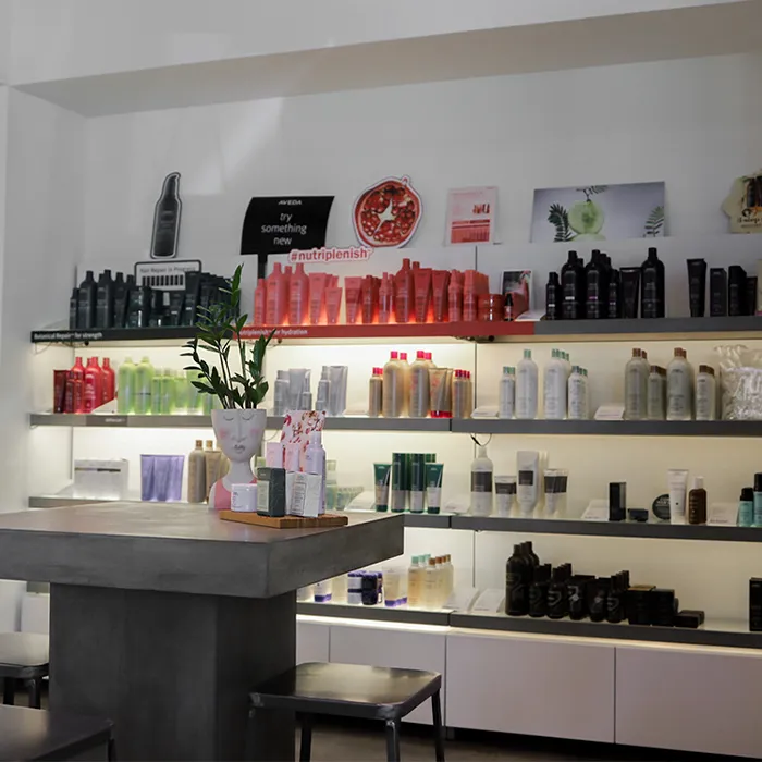 Shelves in a salon display various hair care products and bottles, with a table and chairs in the foreground and decorative items on the table. - Garbo A Salon & Spa TX
